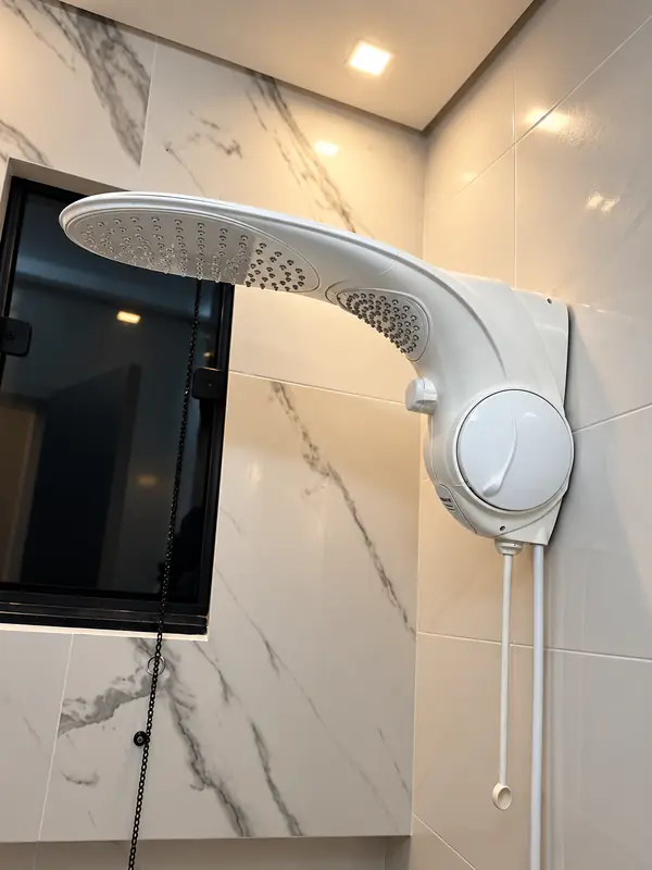 Chuveiro elétrico branco instalado em banheiro com porcelanato marmorizado