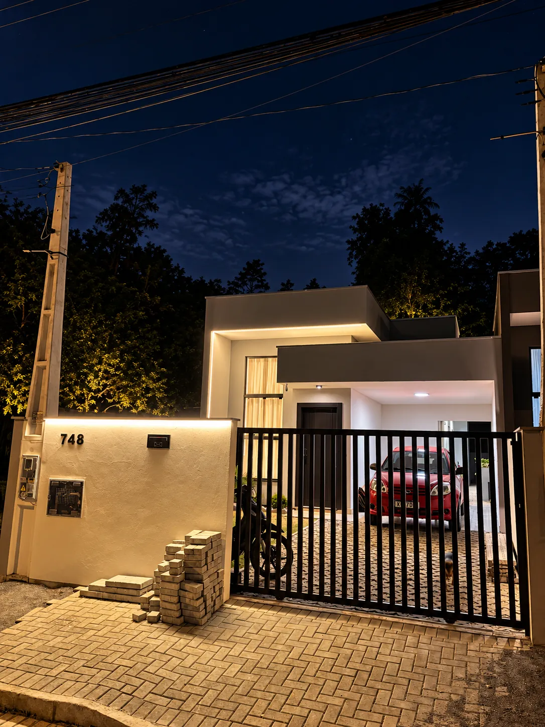 A mesma fachada à noite, com perfis de LED e arandelas acesos